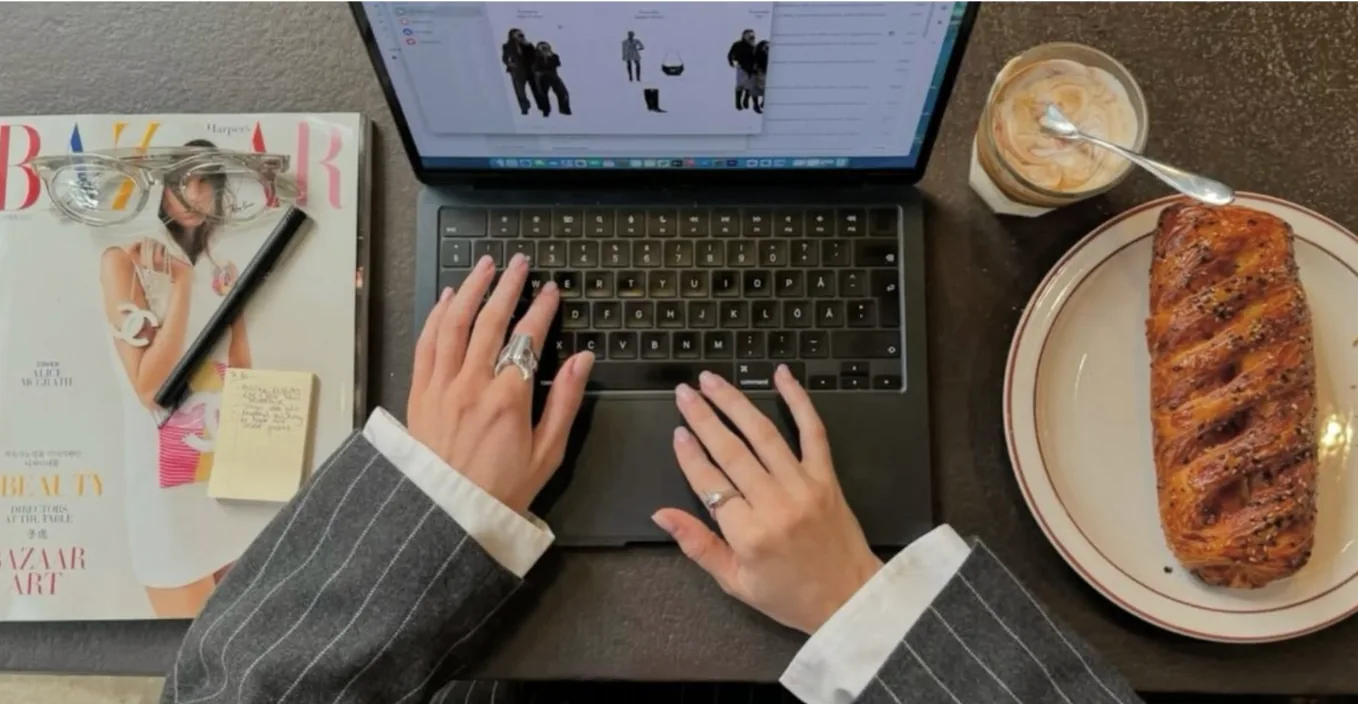 Hands typing on a laptop next to a magazine and pastry