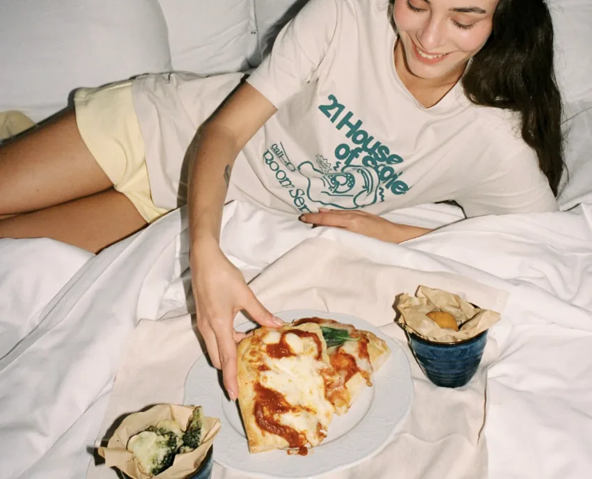 Hand reaching for food on a bed with pink sheets
